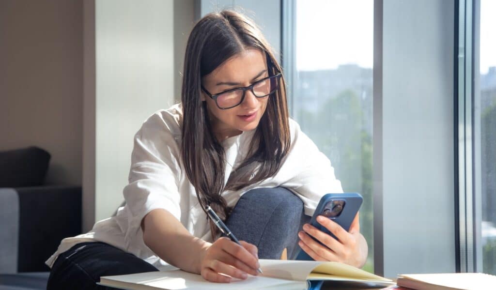 A woman holding a phone while writing